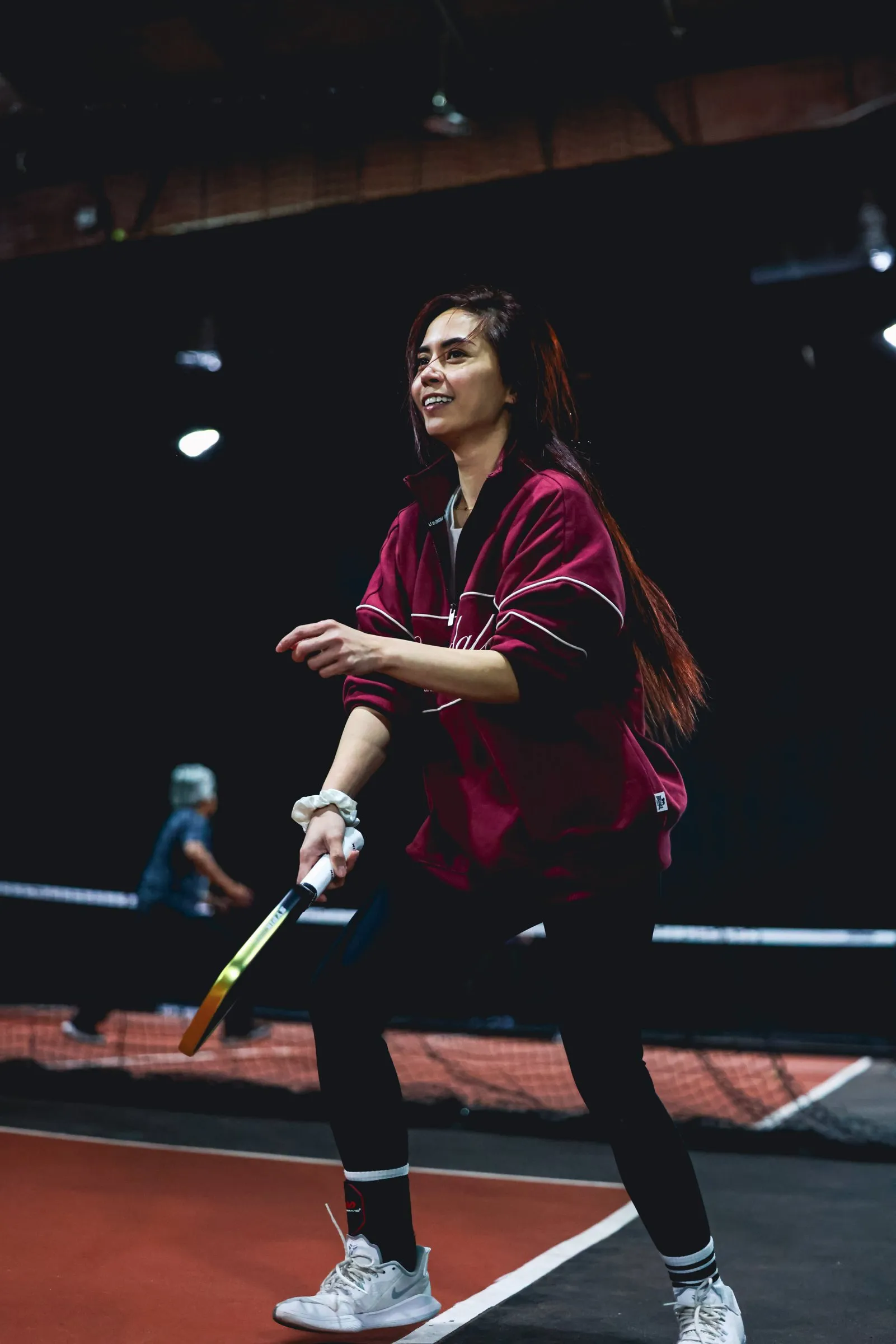 A player smiling mid-rally on a pickleball court at the Park